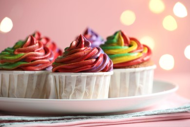 Photo of Delicious cupcakes with colorful cream on table against pink background, closeup. Bokeh effect