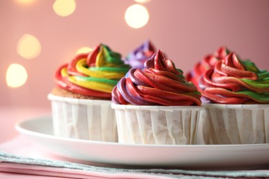 Photo of Delicious cupcakes with colorful cream on table against pink background, closeup. Bokeh effect