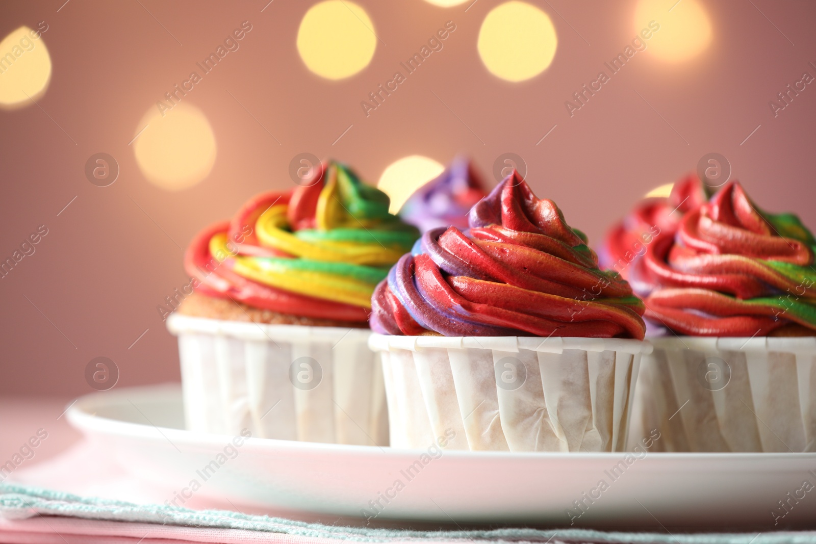 Photo of Delicious cupcakes with colorful cream on table against pink background, closeup. Bokeh effect