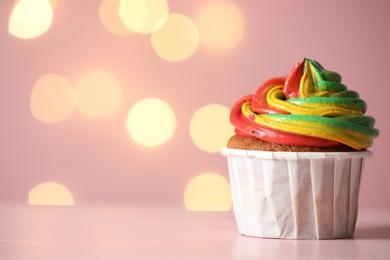 Photo of Delicious cupcake with colorful cream on table against pink background, closeup and space for text. Bokeh effect