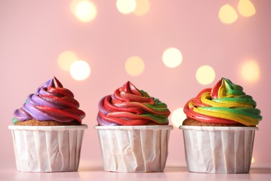 Photo of Delicious cupcakes with colorful cream on table against pink background, closeup and space for text. Bokeh effect