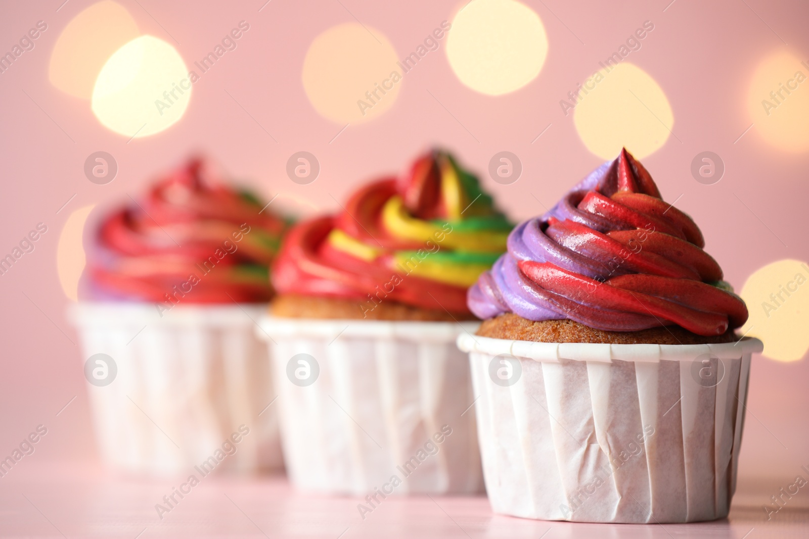 Photo of Delicious cupcakes with colorful cream on table against pink background, closeup. Bokeh effect