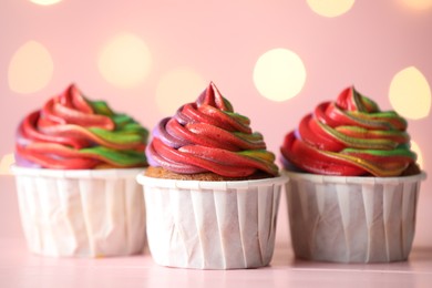 Photo of Delicious cupcakes with colorful cream on table against pink background, closeup. Bokeh effect