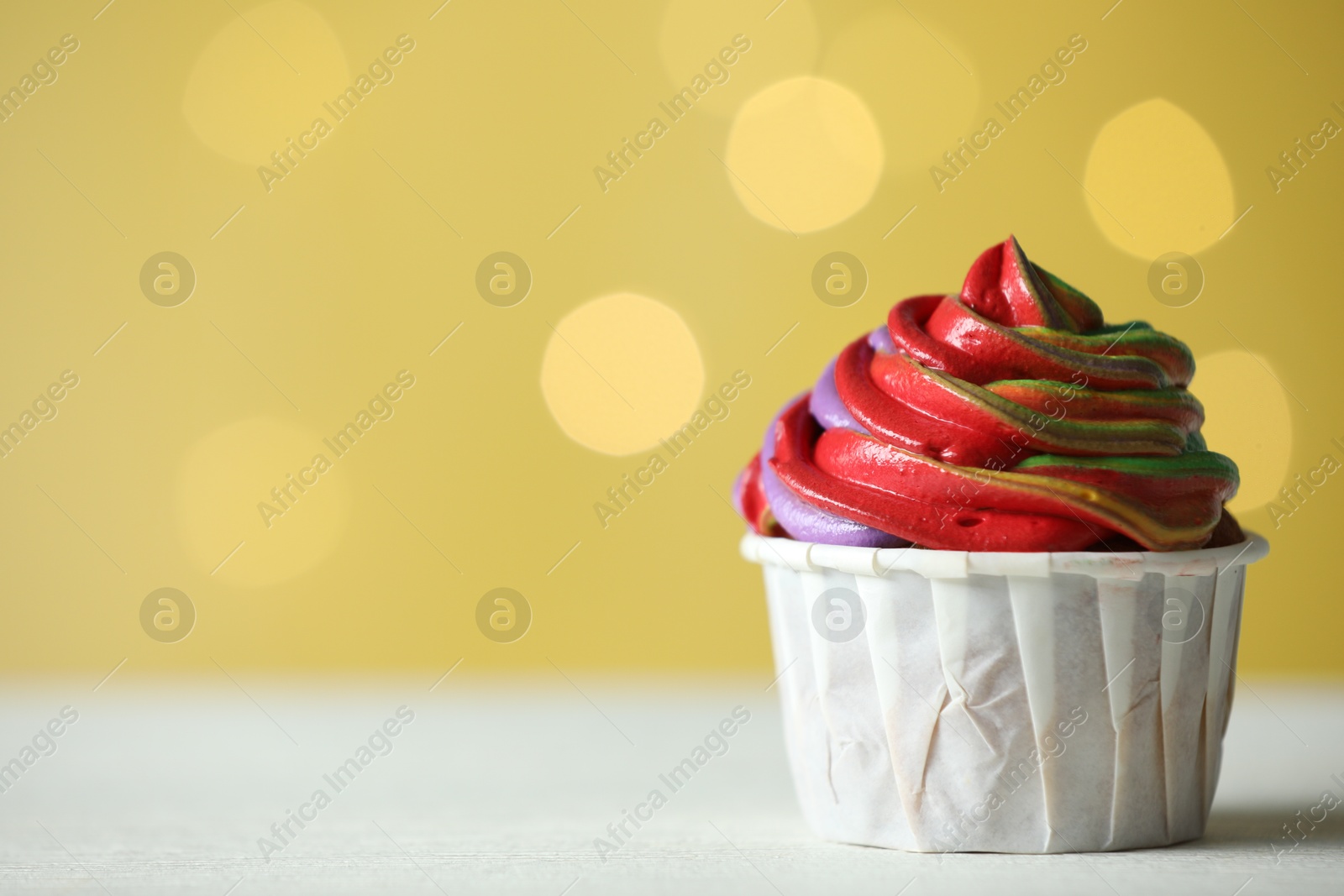 Photo of Delicious cupcake with colorful cream on white table against golden background, closeup and space for text. Bokeh effect