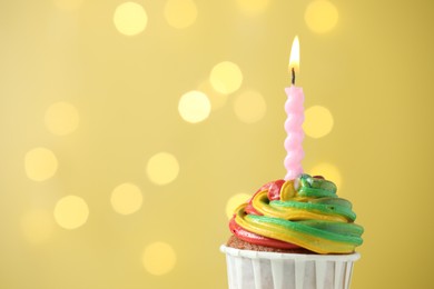 Photo of Delicious cupcake with colorful cream and burning candle against golden background, closeup. Space for text