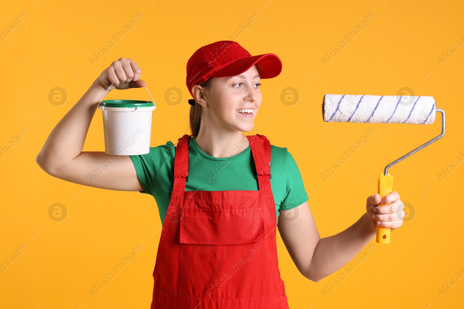 Photo of Professional painter with roller and bucket of paint on orange background