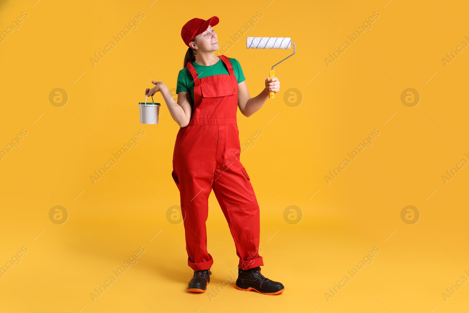 Photo of Professional painter with roller and bucket of paint on orange background