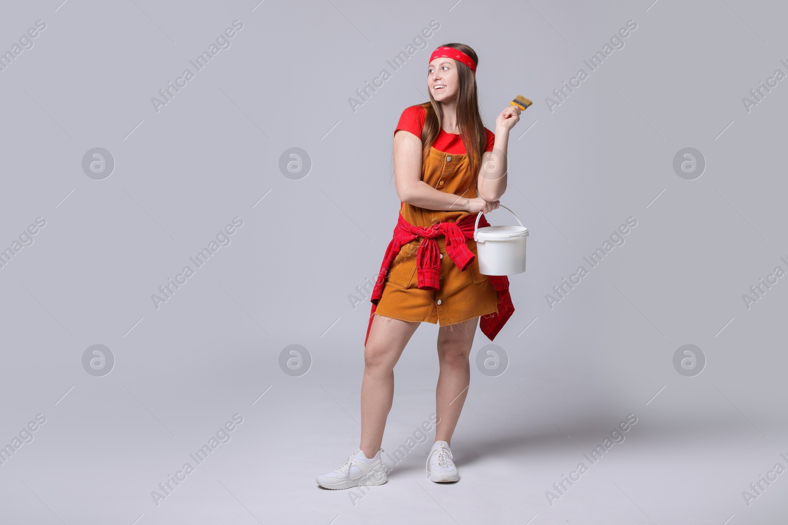 Photo of Woman with brush and bucket of paint on light grey background