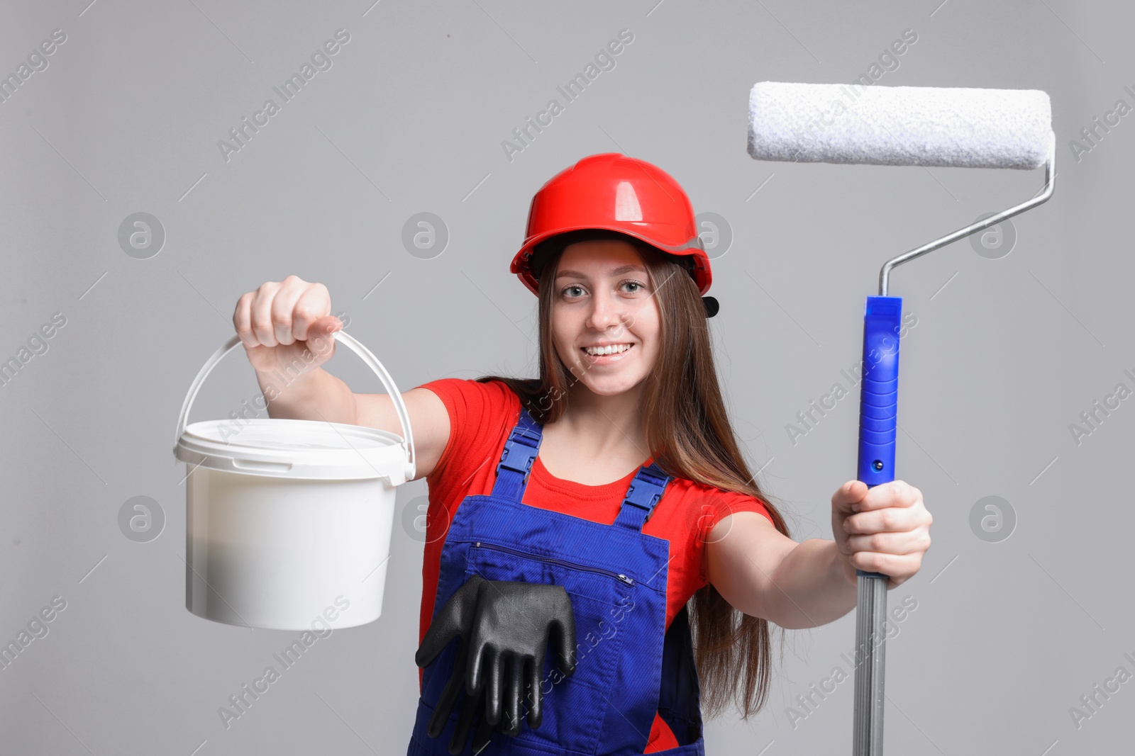 Photo of Professional painter with roller and bucket of paint on light grey background