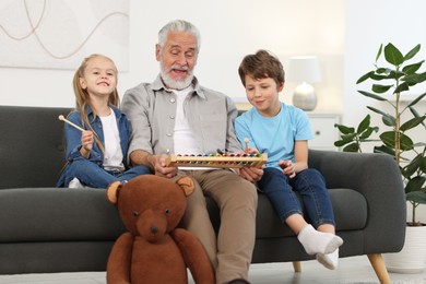 Grandpa and his grandkids playing toy xylophone on sofa at home