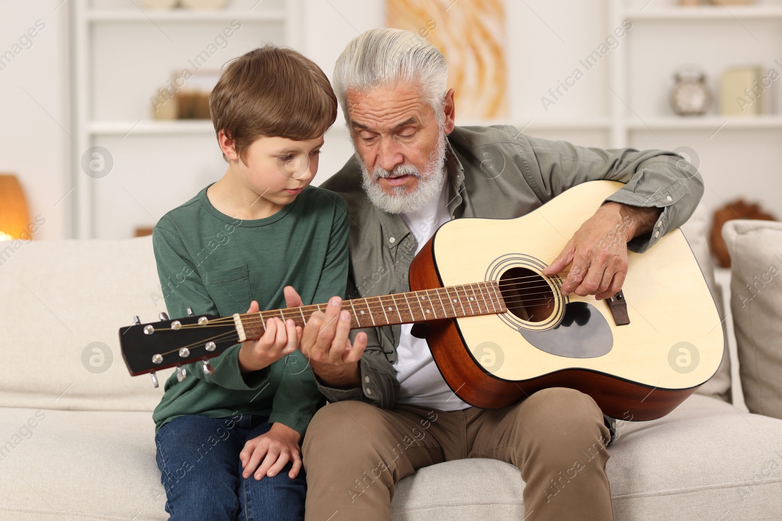 Photo of Grandpa teaching his grandson to play guitar on sofa at home