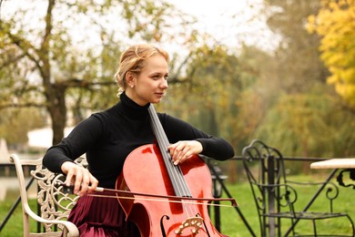 Photo of Beautiful young woman playing cello in park, space for text