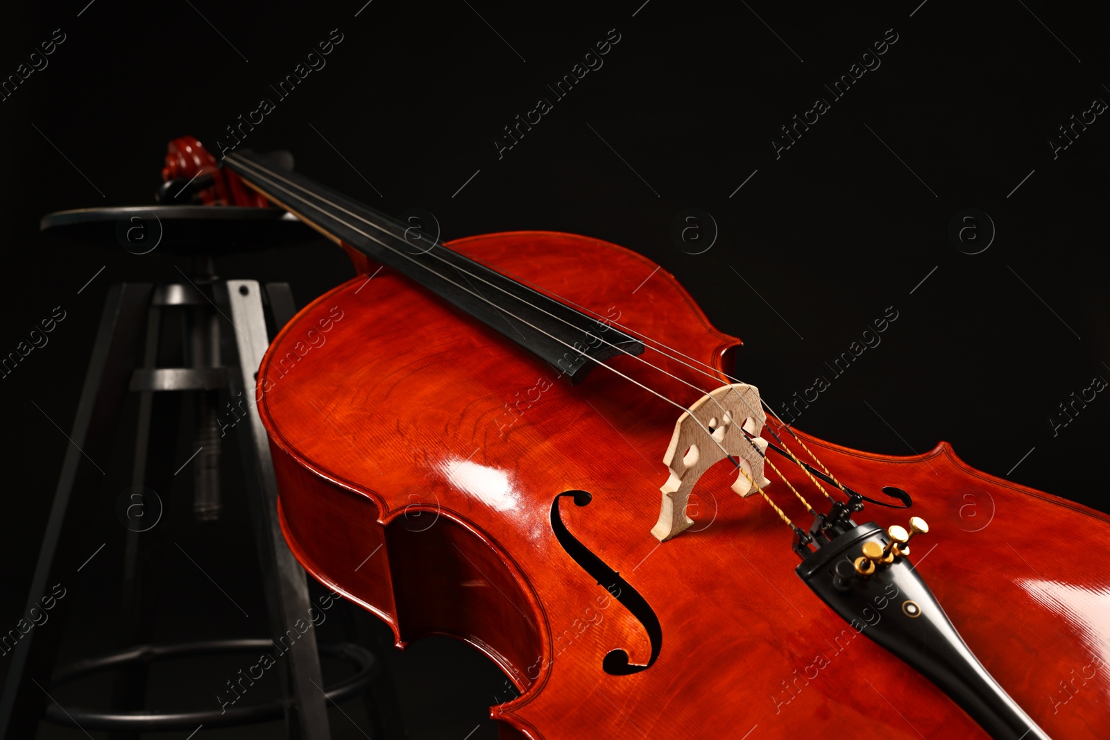 Photo of Beautiful cello and stool on black background. Classic musical instrument