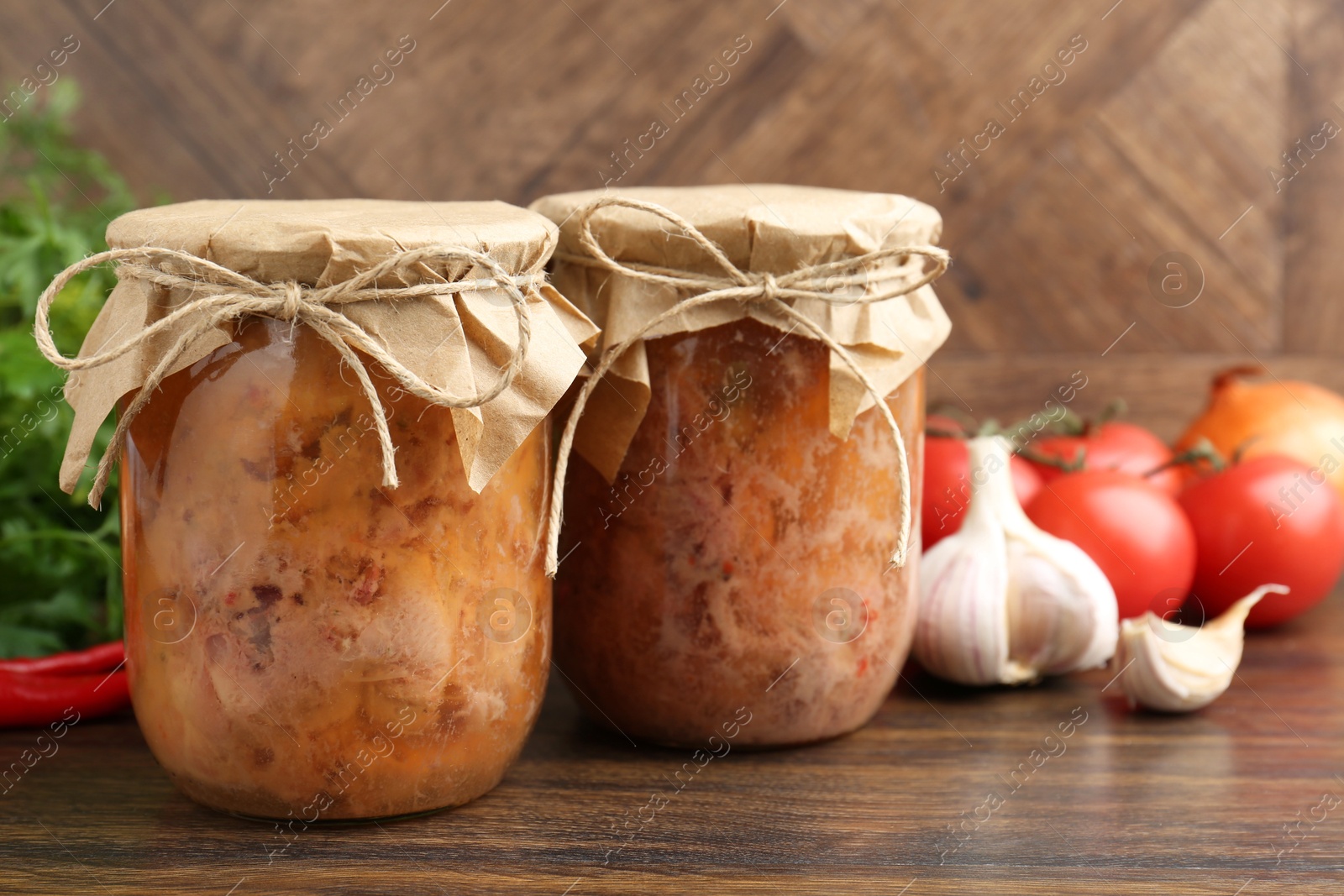 Photo of Canned meat in glass jars and other products on wooden table, closeup