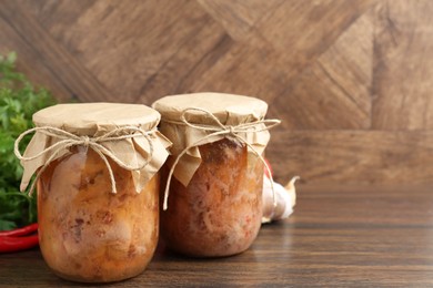 Photo of Canned meat in glass jars on wooden table, space for text