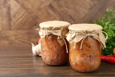 Canned meat in glass jars on wooden table, space for text