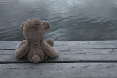 Photo of Lonely teddy bear on deck near river, back view. Space for text