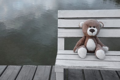 Photo of Lonely teddy bear on bench near river, space for text