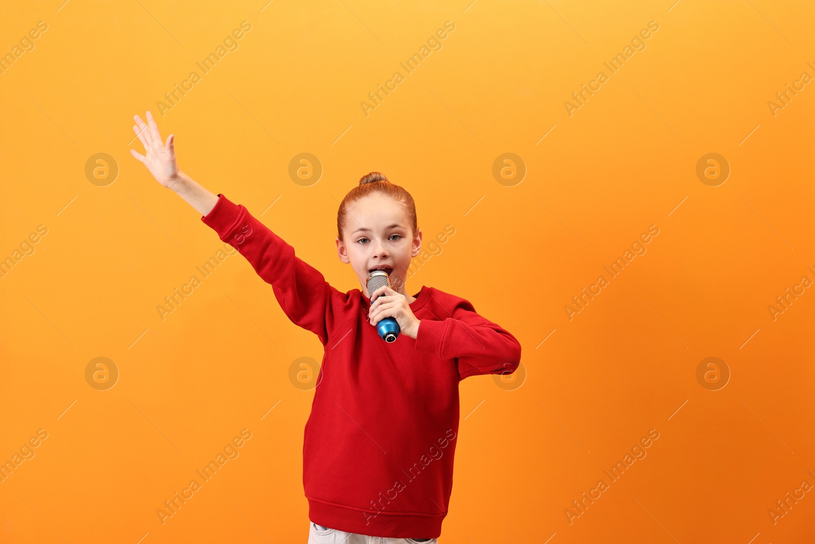 Photo of Little girl with microphone singing on orange background