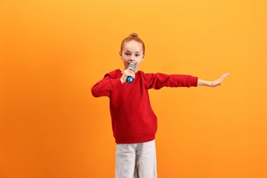 Photo of Little girl with microphone singing on orange background