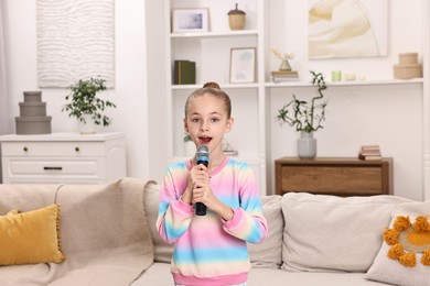 Photo of Little girl with microphone singing near sofa at home