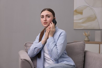 Stressed woman calling hotline for mental health help in armchair at home