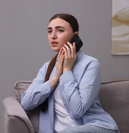 Photo of Stressed woman calling hotline for mental health help in armchair at home. Space for text