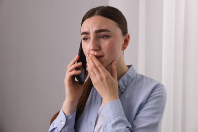 Stressed woman calling hotline for mental health help near window at home