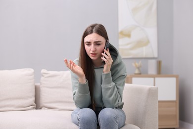 Photo of Depressed woman calling hotline for mental health help on sofa at home