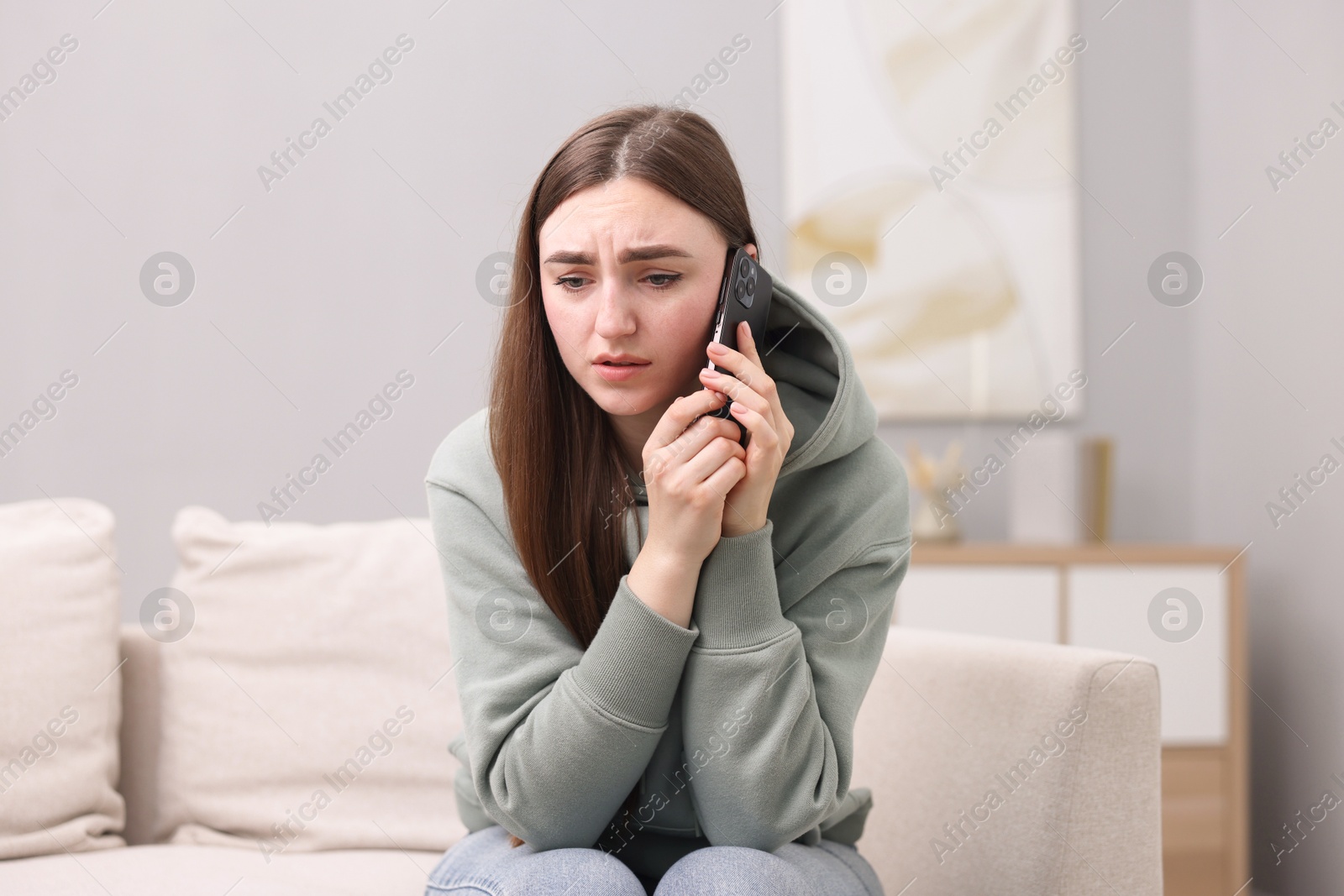 Photo of Depressed woman calling hotline for mental health help on sofa at home