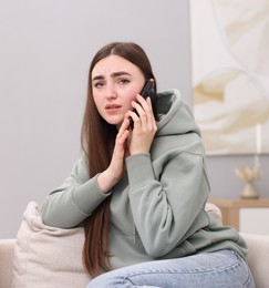 Depressed woman calling hotline for mental health help on sofa at home