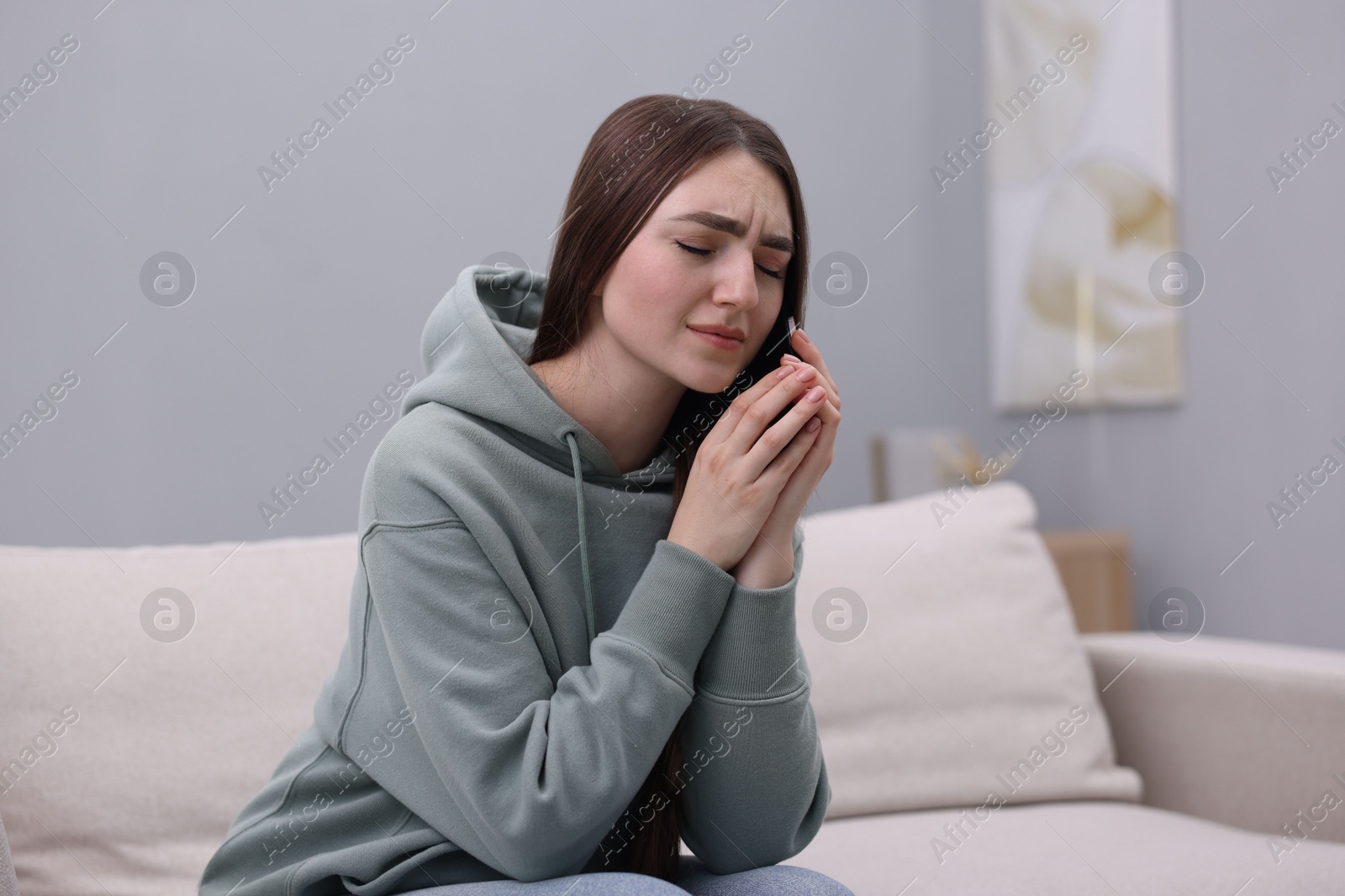 Photo of Depressed woman calling hotline for mental health help on sofa at home