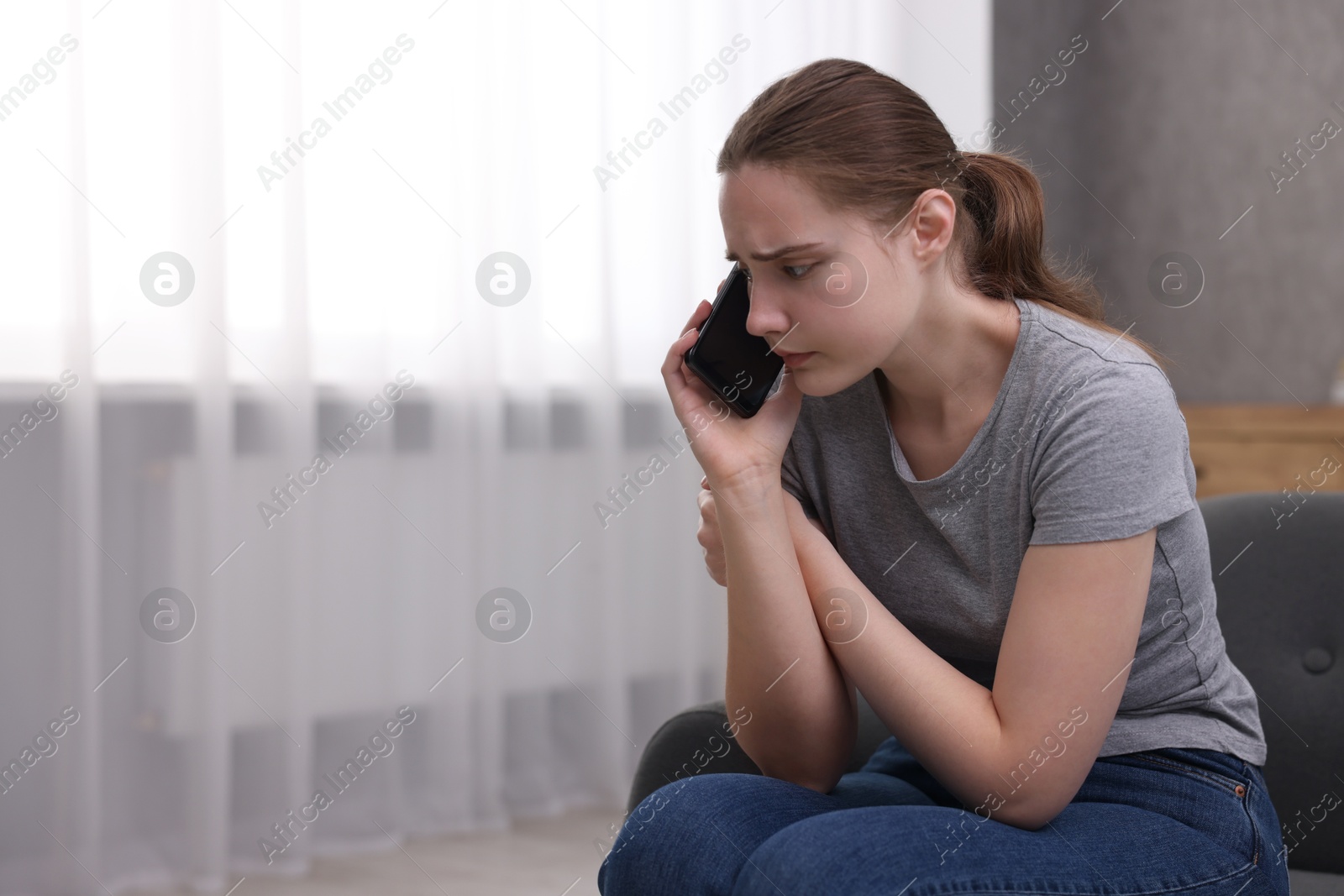 Photo of Depressed woman calling hotline for mental health help on sofa at home. Space for text