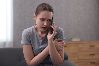 Photo of Depressed woman calling hotline for mental health help on sofa at home. Space for text