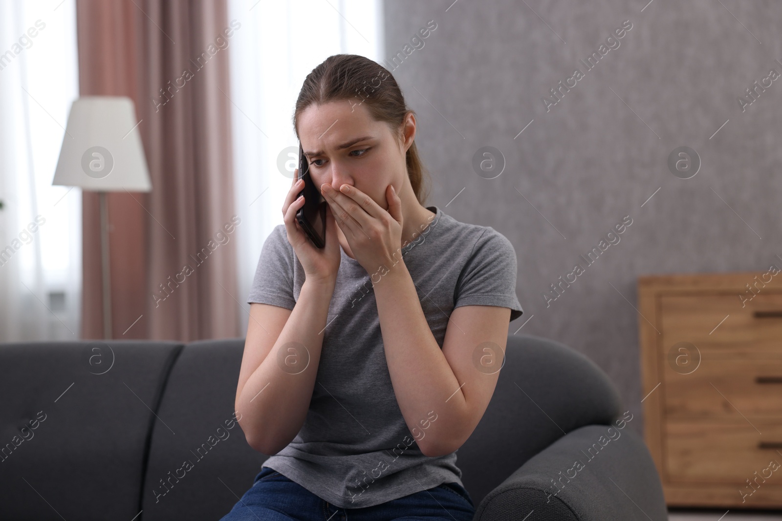 Photo of Depressed woman calling hotline for mental health help on sofa at home