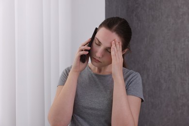 Photo of Stressed woman calling hotline for mental health help near window at home