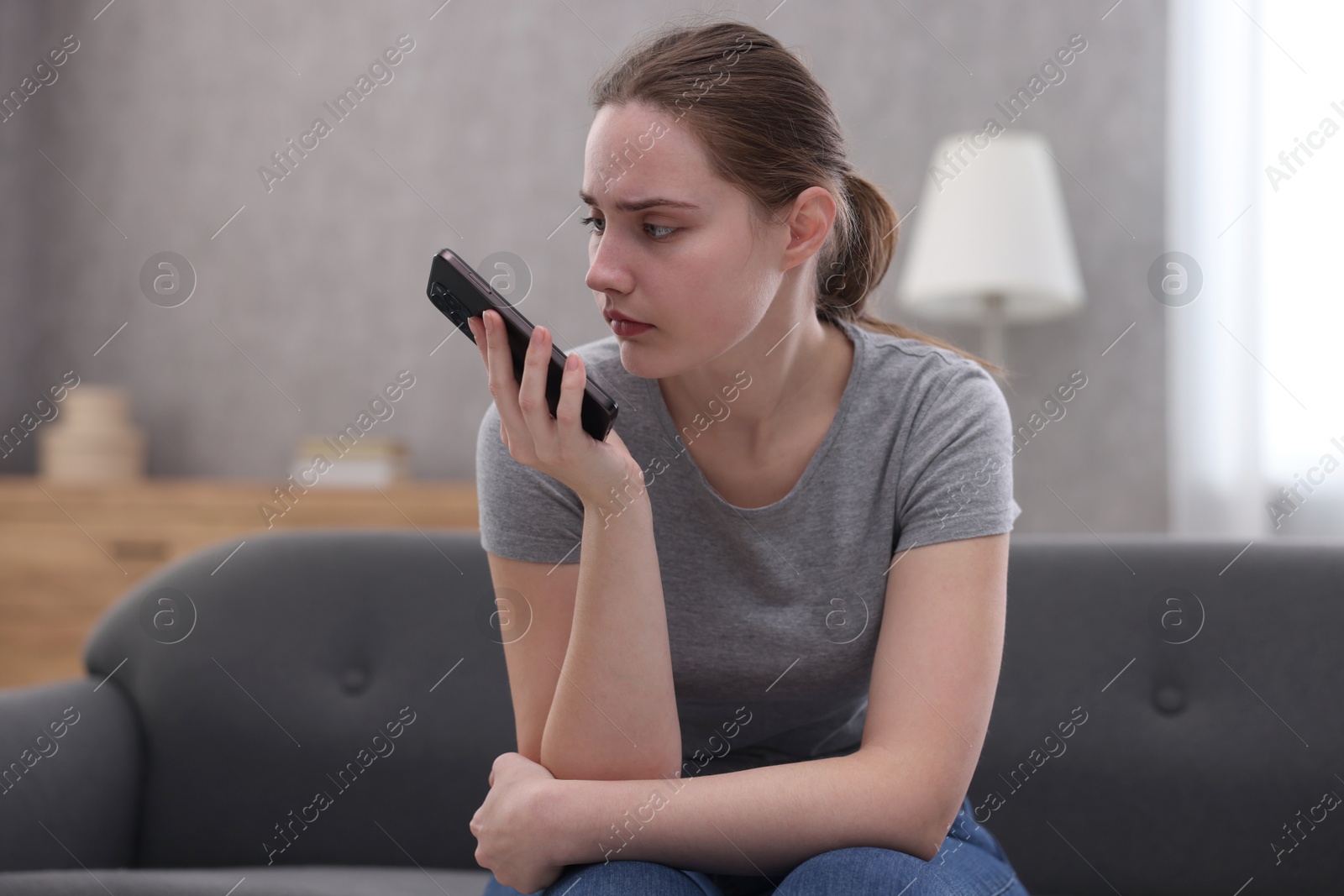 Photo of Depressed woman calling hotline for mental health help on sofa at home