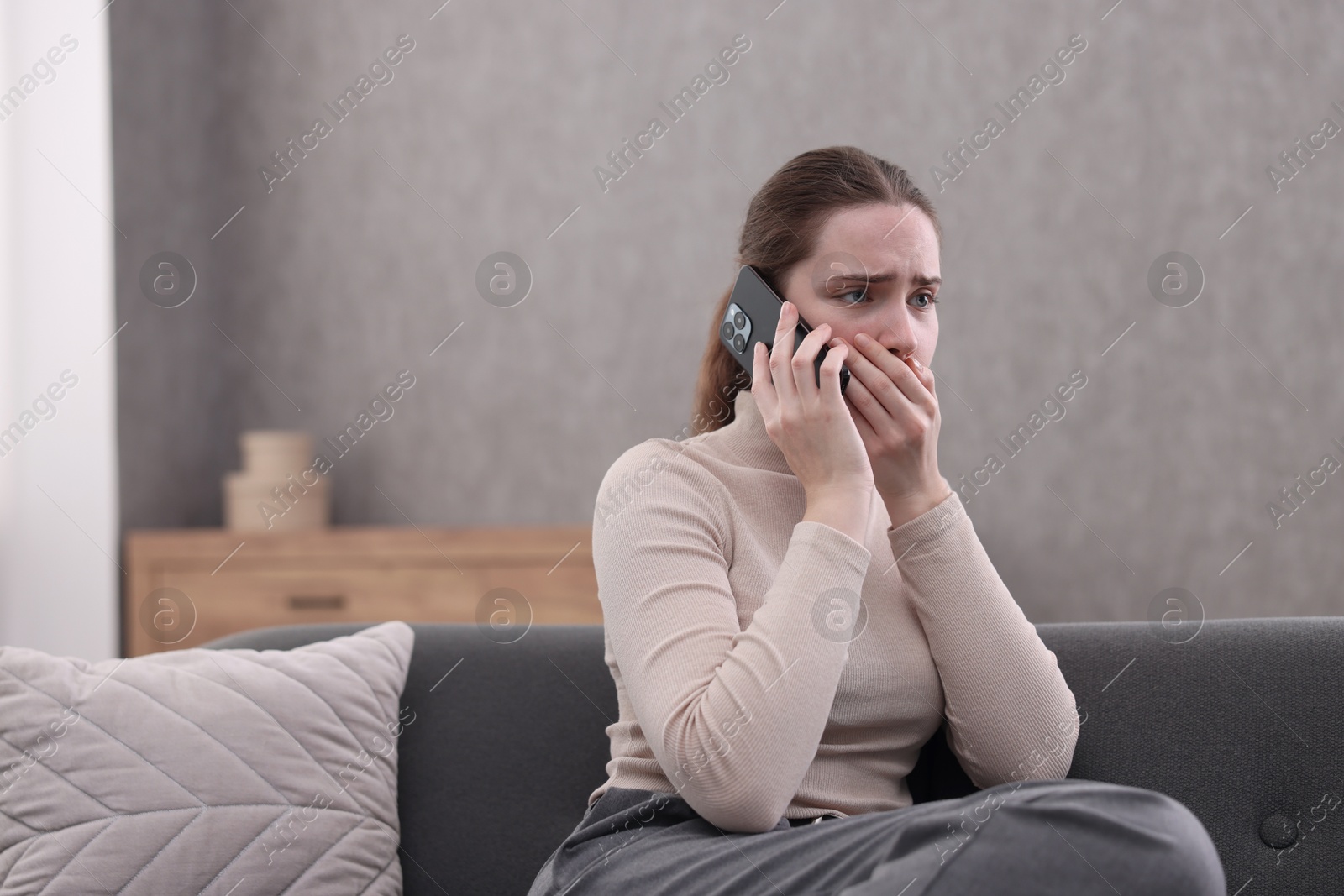 Photo of Depressed woman calling hotline for mental health help on sofa at home