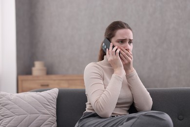 Depressed woman calling hotline for mental health help on sofa at home