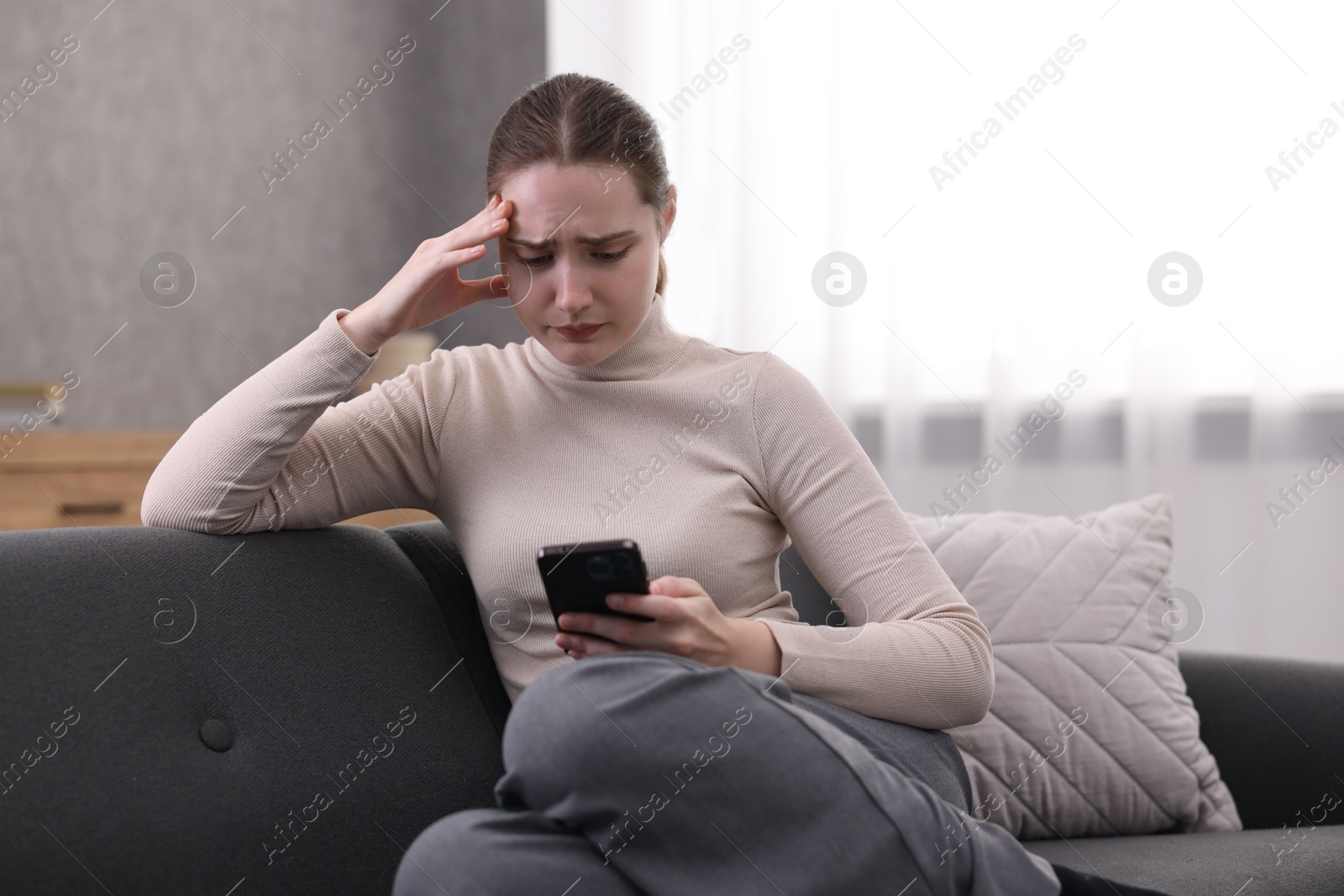 Photo of Depressed woman calling hotline for mental health help on sofa at home