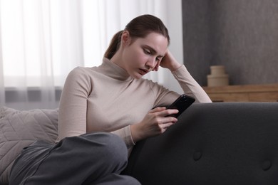 Photo of Depressed woman calling hotline for mental health help on sofa at home