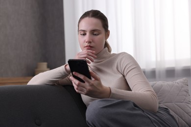 Photo of Depressed woman calling hotline for mental health help on sofa at home