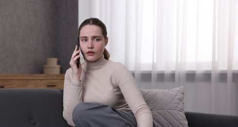 Photo of Depressed woman calling hotline for mental health help on sofa at home. Space for text