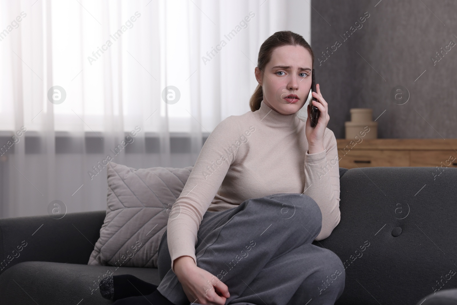 Photo of Depressed woman calling hotline for mental health help on sofa at home