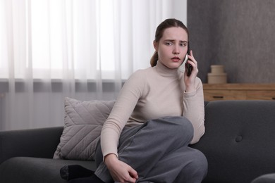 Photo of Depressed woman calling hotline for mental health help on sofa at home