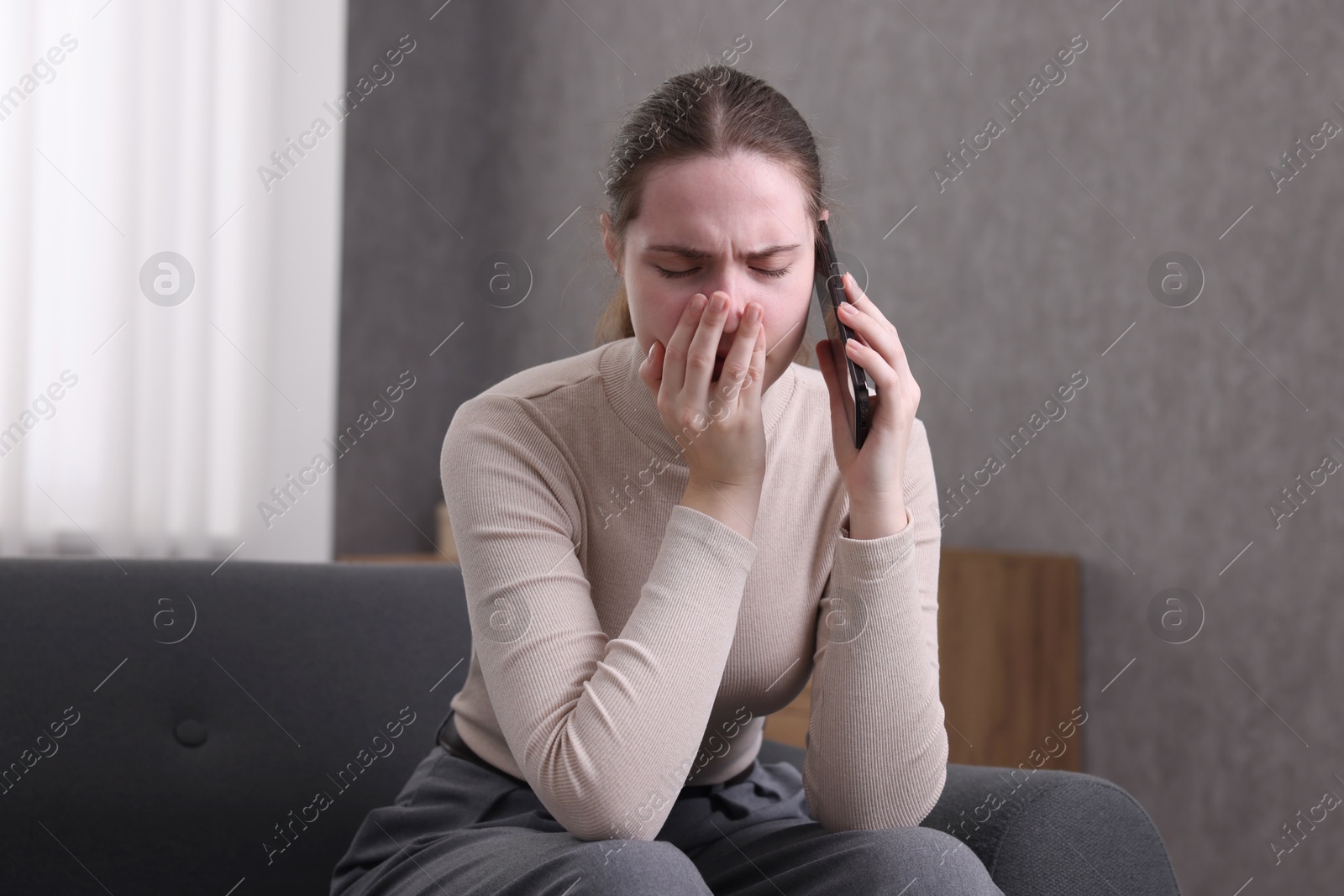 Photo of Depressed woman calling hotline for mental health help on sofa at home