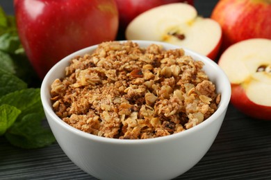 Photo of Delicious apple crisp in bowl, fresh fruits and mint on black textured table, closeup