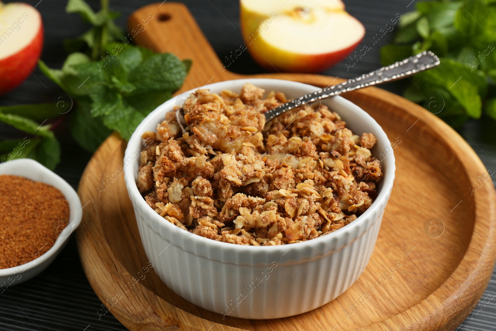 Photo of Delicious apple crisp in bowl and ingredients on table, closeup