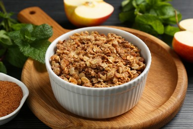 Photo of Delicious apple crisp in bowl and ingredients on black table, closeup