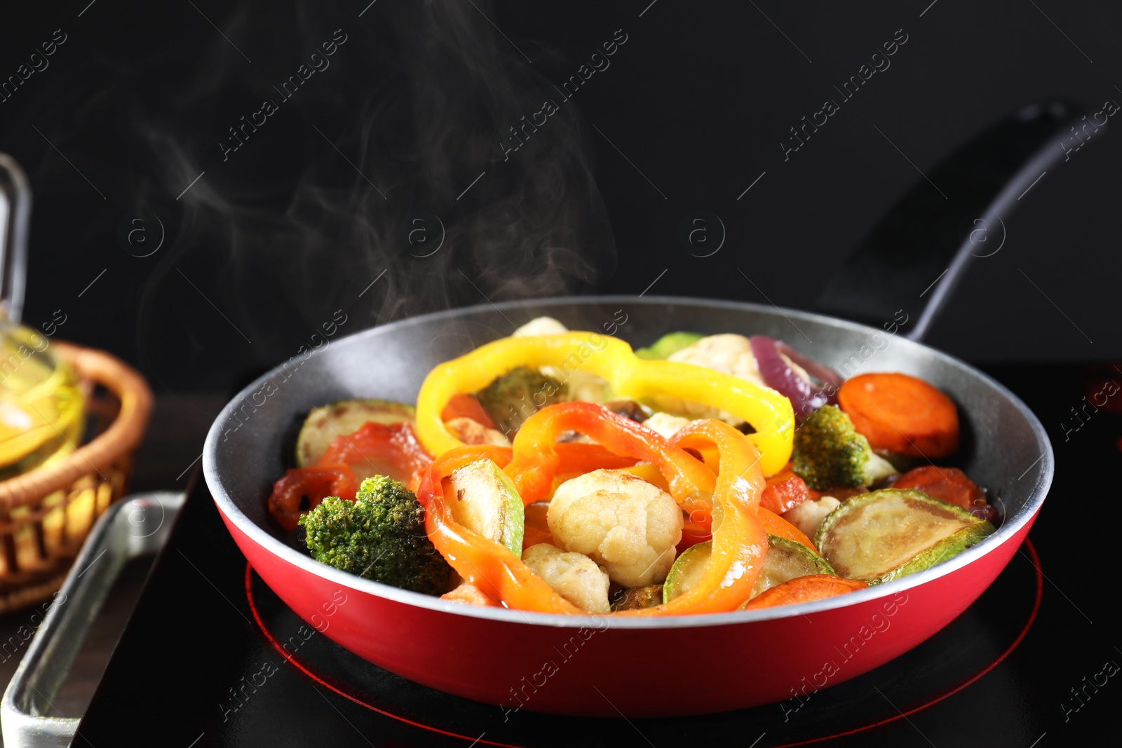 Photo of Frying pan with vegetables and stove on table against black background, closeup